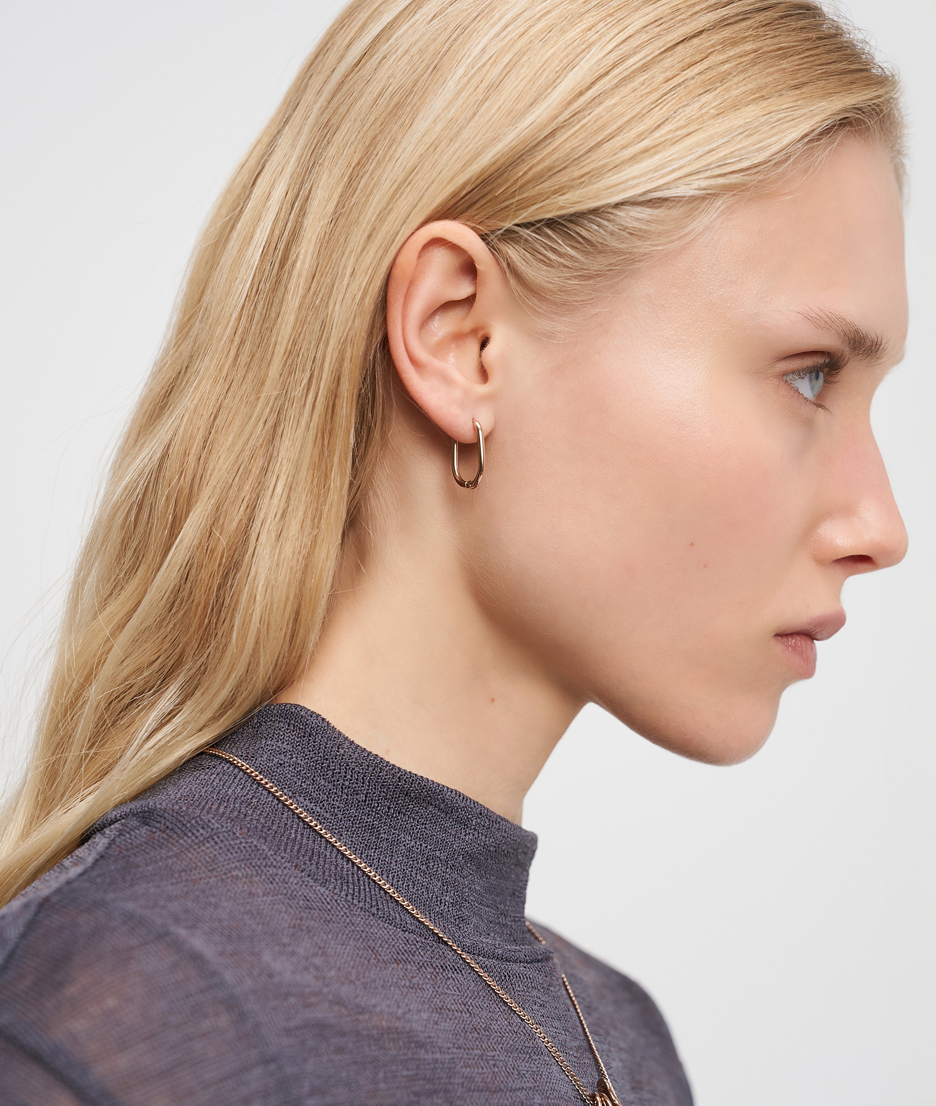 Eine Frau mit langen blonden Haaren trägt den Liebeskind Berlin Ohrring - Organic Shapes als modernes Accessoire zu einem grauen Oberteil, dargestellt im Profil vor weißem Hintergrund.