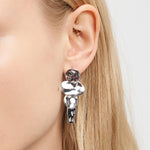 Nahaufnahme eines Frauenohrs, das den Liebeskind Berlin Ohrring - Organic Shapes trägt, einen großen abstrakten silbernen und schwarzen Statement-Ohrring von Liebeskind Berlin.