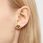 Nahaufnahme eines Frauenohrs mit drei goldenen Liebeskind Berlin Ohrringen - Organic Shapes: ein großer runder Ohrstecker und zwei kleine spiralförmige Ohrstecker - ein elegantes Stück von Liebeskind Berlin für jede Gelegenheit.