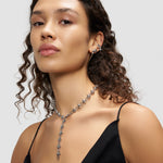 Frau mit lockigem Haar trägt ein schwarzes Oberteil und silbernen Schmuck mit Spikes, darunter die Liebeskind Berlin Halskette - Spikes und auffällige Ohrringe - ein echter Statement-Look.