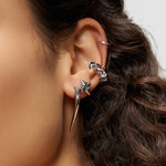Nahaufnahme eines Ohrs, das mit silbernen Ohrringen geschmückt ist - einem großen Spike, kleinen Creolen, Ohrsteckern und dem LIEBESKIND BERLIN Earcuff - Spikes von Liebeskind Berlin, einem stilvollen Accessoire, das urbanes Design zeigt.