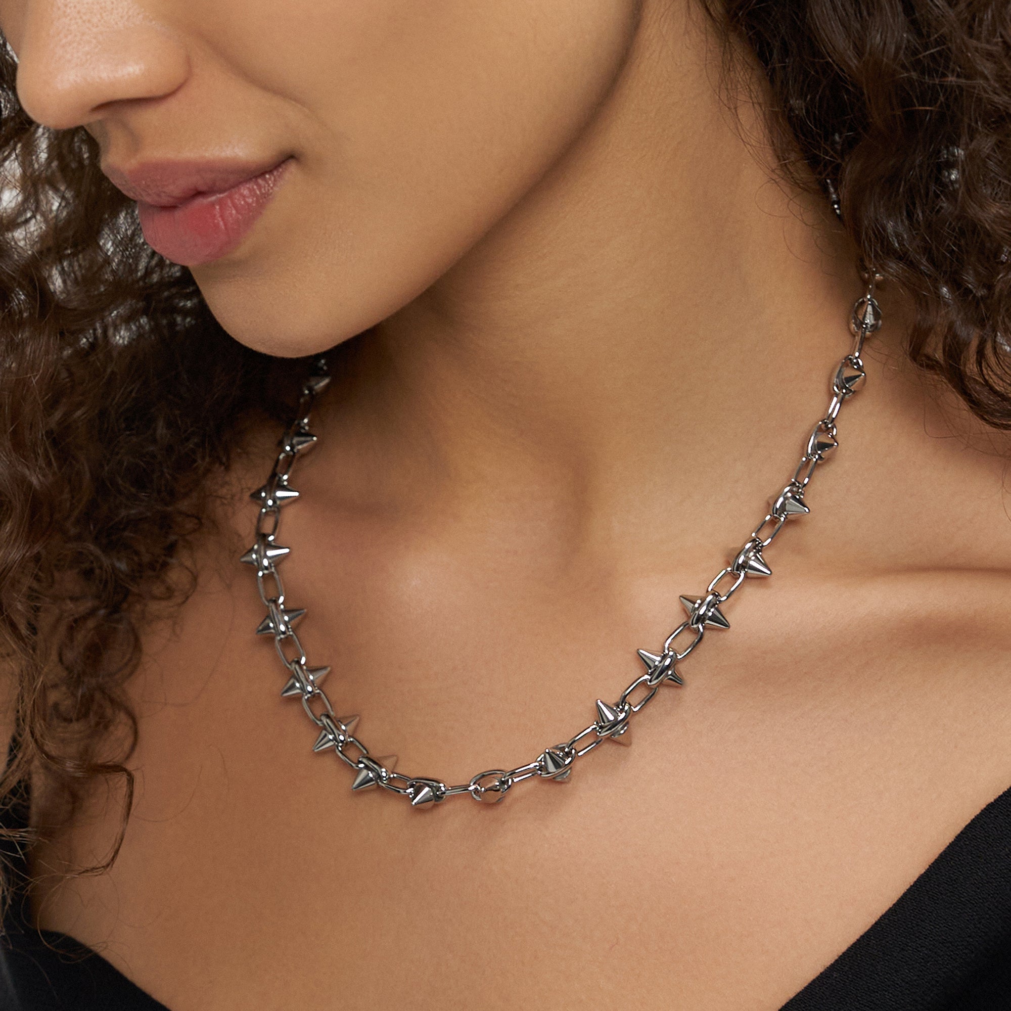 Eine Frau mit schwarzem Oberteil trägt die LIEBESKIND BERLIN Halskette - Spikes von Liebeskind Berlin, eine silberne Kette mit Stacheln, und hat ihr gewelltes Haar über eine Seite drapiert.