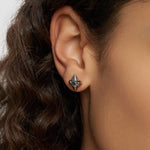 Nahaufnahme eines Frauenohrs mit lockigem Haar, das einen Liebeskind Berlin Ohrstecker - Spikes trägt, einen metallischen, kegelförmigen Ohrring mit Spike-Muster und Silikonverschluss.