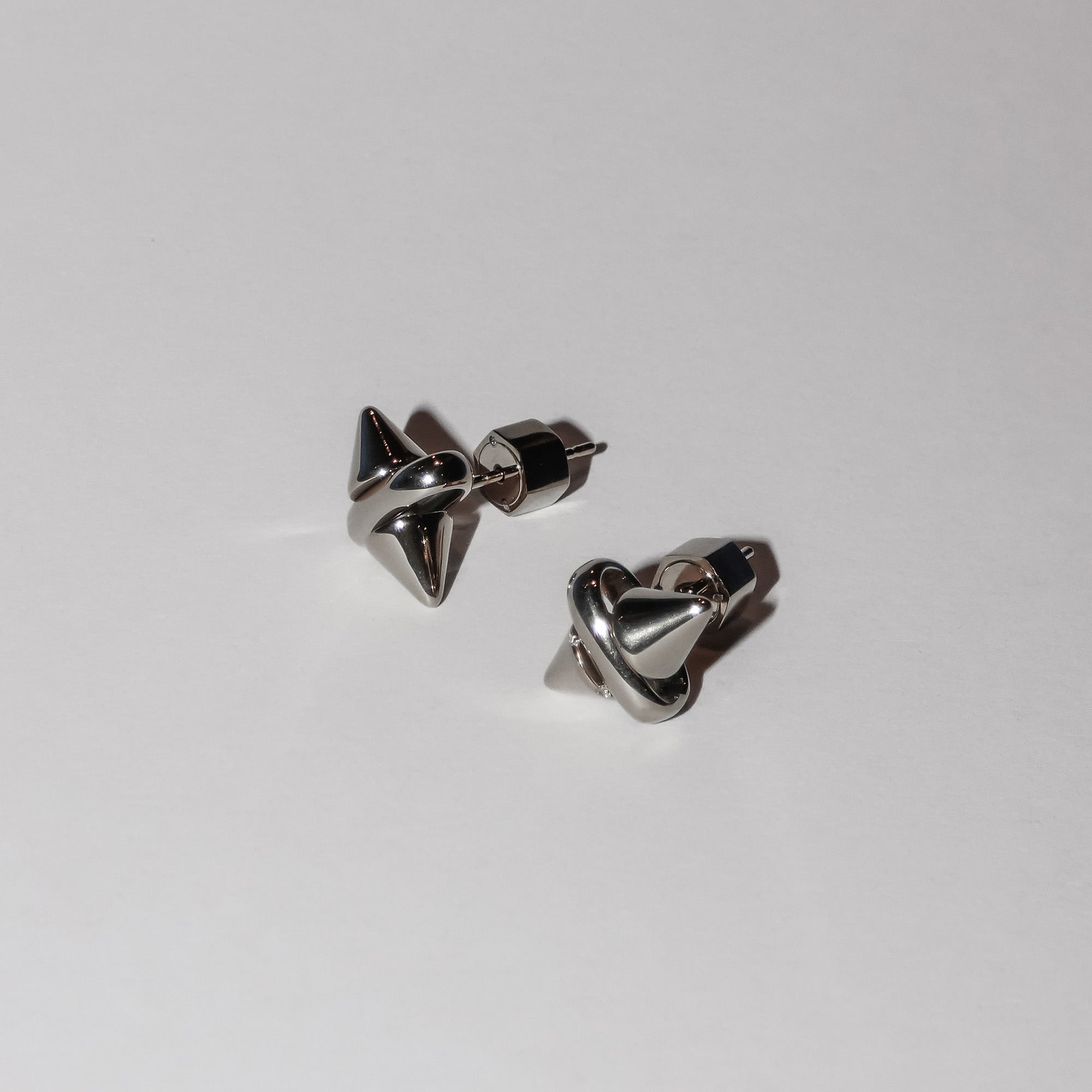 Ein Paar LIEBESKIND BERLIN Ohrstecker - Spikes von Liebeskind Berlin mit glänzendem, geometrischem Design, Silikonverschluss und dezentem Spikes-Muster wird auf einem schlichten weißen Hintergrund präsentiert.