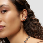 Frau mit lockigem Haar trägt mehrere silberne Ohrringe, darunter den LIEBESKIND BERLIN Earcuff - Spikes von Liebeskind Berlin, und eine Stachelhalskette - ein urbaner, stilvoller Look in Nahaufnahme.