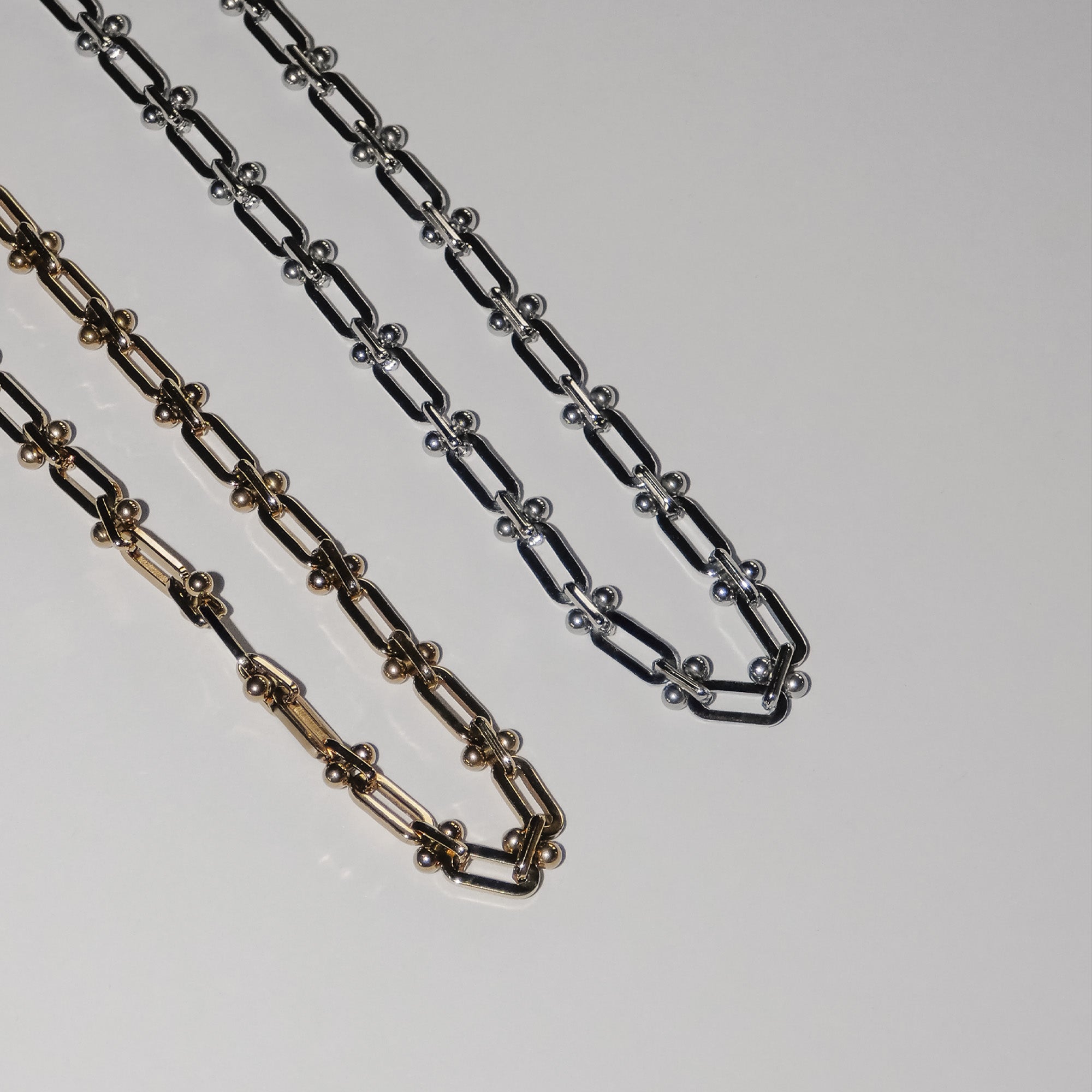 Zwei Metallketten - eine goldene und eine silberne LIEBESKIND BERLIN Halskette - Urban Chic von Liebeskind Berlin - liegen nebeneinander auf weißem Grund.