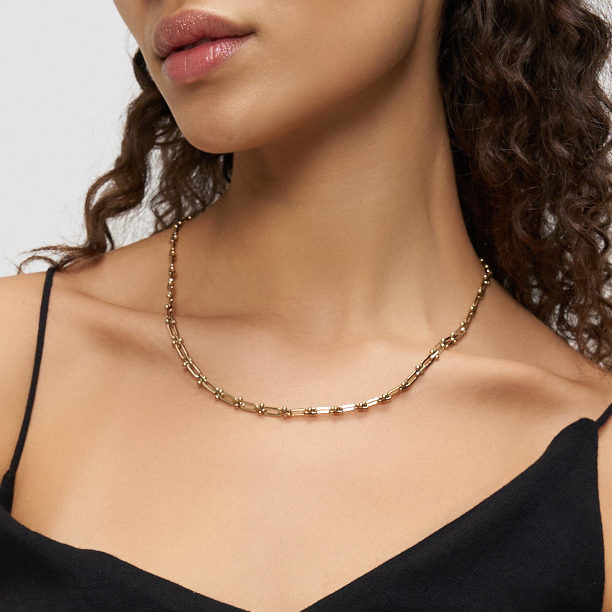 Frau trägt ein ärmelloses schwarzes Oberteil und die LIEBESKIND BERLIN Halskette - Urban Chic, eine goldene Kette von Liebeskind Berlin mit rechteckigen und stabförmigen Gliedern, die als schicke Y-Kette gestaltet ist.