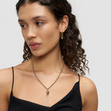Frau in einem schwarzen Oberteil, die eine Liebeskind Berlin Halskette - Metal Heart und dazu passende Damen Schmuck Ohrringe trägt und nach links schaut.