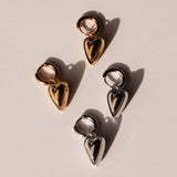 Zwei Paar LIEBESKIND BERLIN Creole - Metal Heart Creolen, eine in Gold und eine in Silber, auf hellem Grund - eleganter Schmuck von Liebeskind Berlin.
