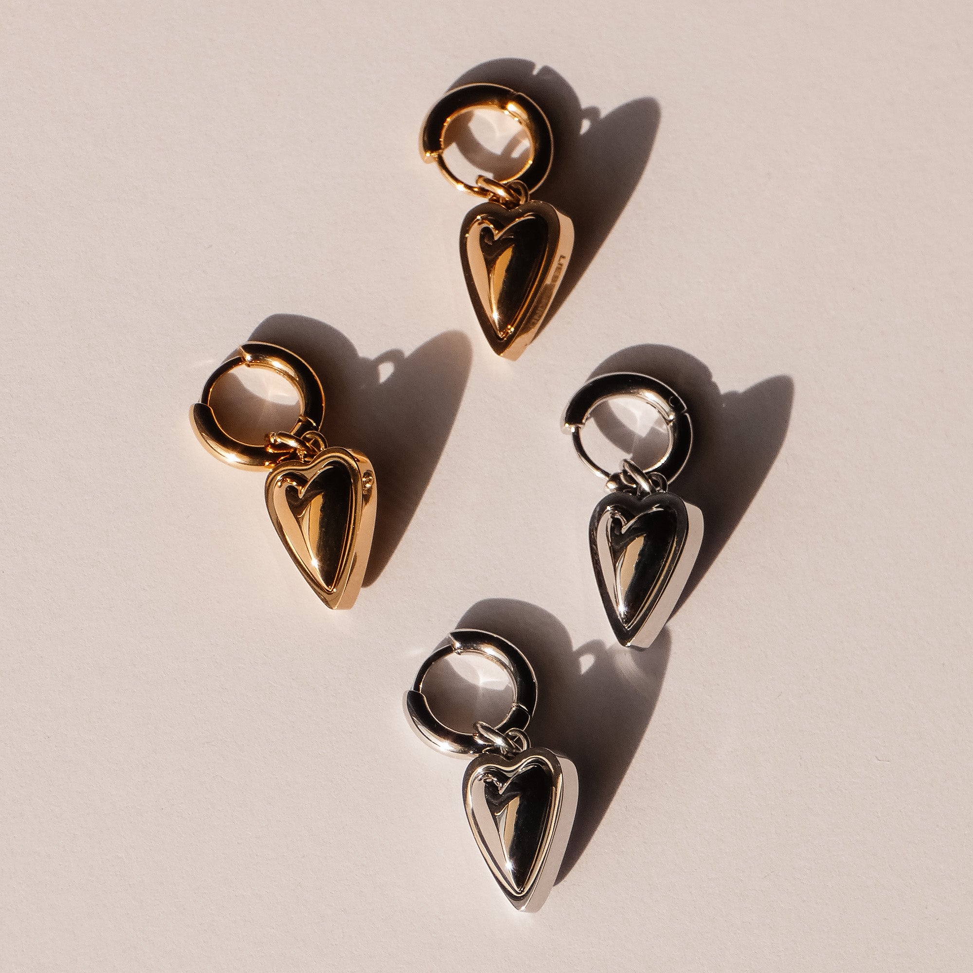 Zwei Paar LIEBESKIND BERLIN Creole - Metal Heart Creolen, eine in Gold und eine in Silber, auf hellem Grund - eleganter Schmuck von Liebeskind Berlin.