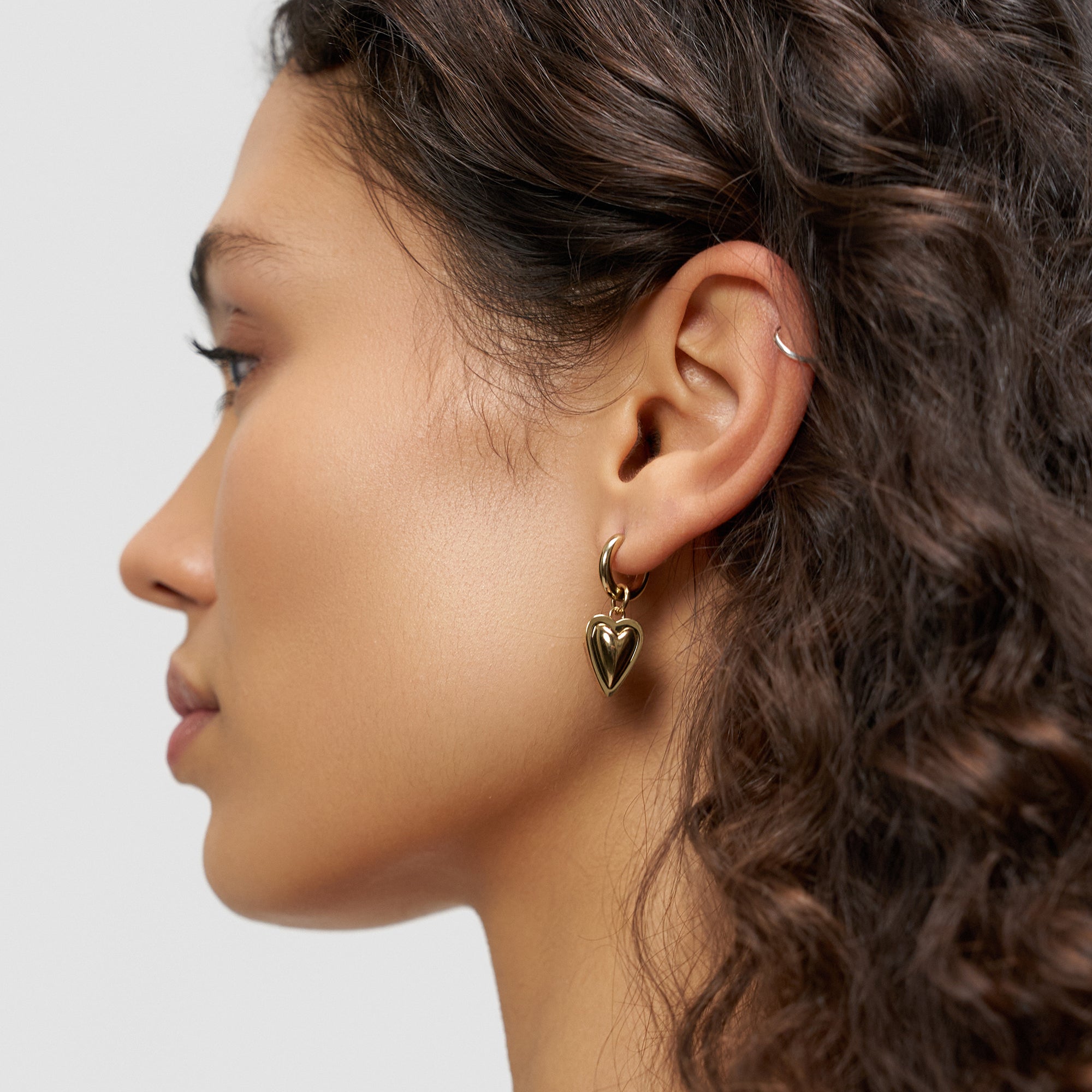 Frau mit lockigem Haar trägt einen Liebeskind Berlin LIEBESKIND BERLIN Creole - Metal Heart Ohrring und eine silberne Ohrmanschette, dargestellt in Profilansicht.