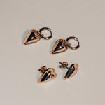 LIEBESKIND BERLIN Creole - Metal Heart Ohrringe von Liebeskind Berlin: goldene und schwarze herzförmige Creolen und Ohrstecker mit Herzanhänger-Details, gezeigt auf neutralem Hintergrund für einen modernen urbanen Look.