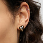 Nahaufnahme eines Ohres mit dem glänzenden LIEBESKIND BERLIN Ohrstecker - Metal Heart gold von Liebeskind Berlin und einem dünnen silbernen Reif am oberen Ohr für ein schickes Schmuckstatement.