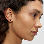 Eine Frau mit lockigem Haar trägt einen kleinen Liebeskind Berlin Ohrstecker - Metal Heart in ihrem linken Ohr, dargestellt in einer Nahaufnahme im Seitenprofil.