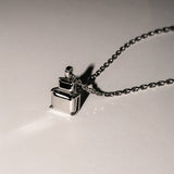 Die LIEBESKIND BERLIN Halskette - Steel Diamond von Liebeskind Berlin mit ihrem geometrischen, minimalistischen Anhänger wirft einen Schatten auf eine schlichte Oberfläche.