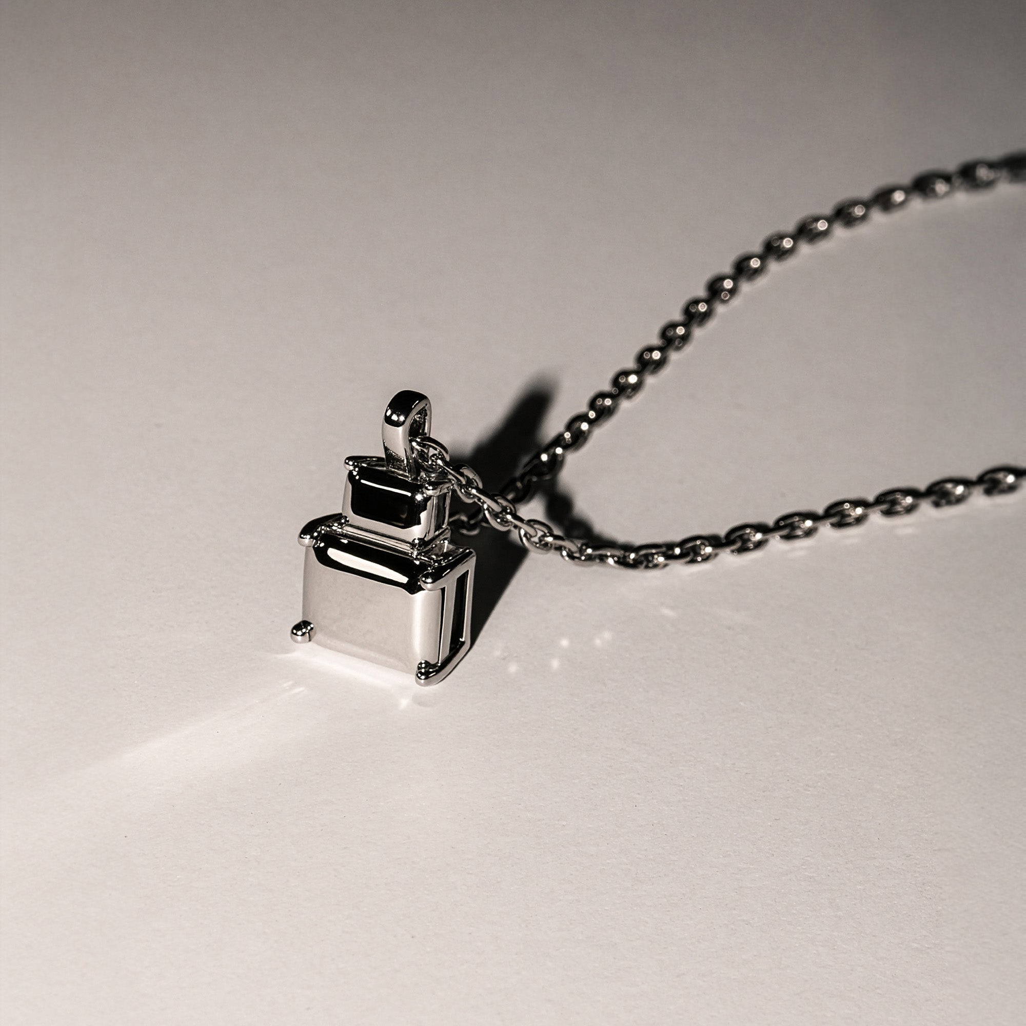 Die LIEBESKIND BERLIN Halskette - Steel Diamond von Liebeskind Berlin mit ihrem geometrischen, minimalistischen Anhänger wirft einen Schatten auf eine schlichte Oberfläche.