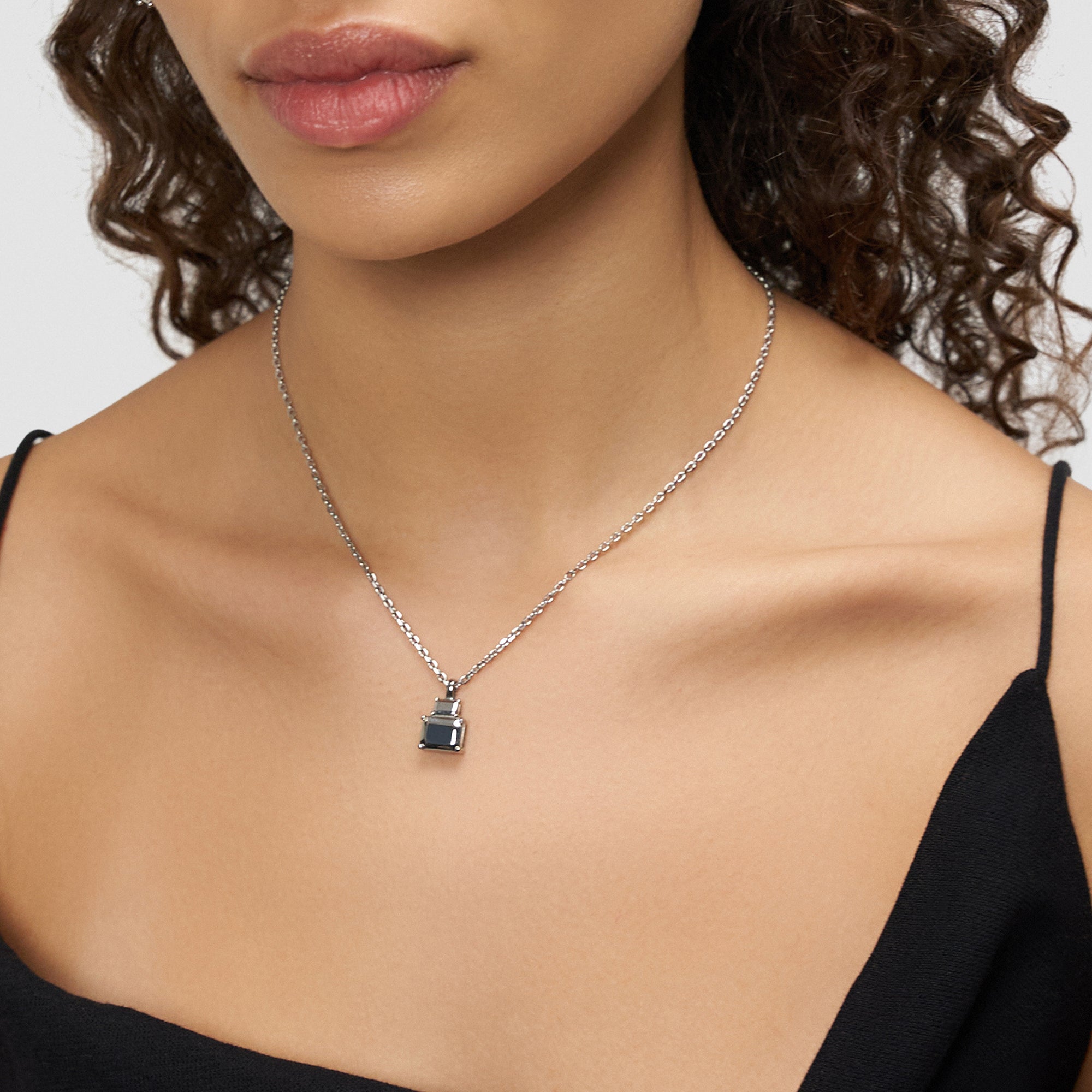 Eine Frau trägt die Liebeskind Berlin Halskette - Steel Diamond mit einem quadratischen Anhänger in schwarzer Diamantenoptik zu einem schwarzen Spaghettiträger-Top.