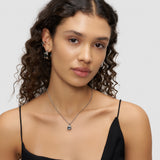 Frau mit gewelltem Haar trägt ein schwarzes Oberteil, den Liebeskind Berlin LIEBESKIND BERLIN Earcuff - Steel Diamond und eine passende Edelstahlkette und schaut in die Kamera.