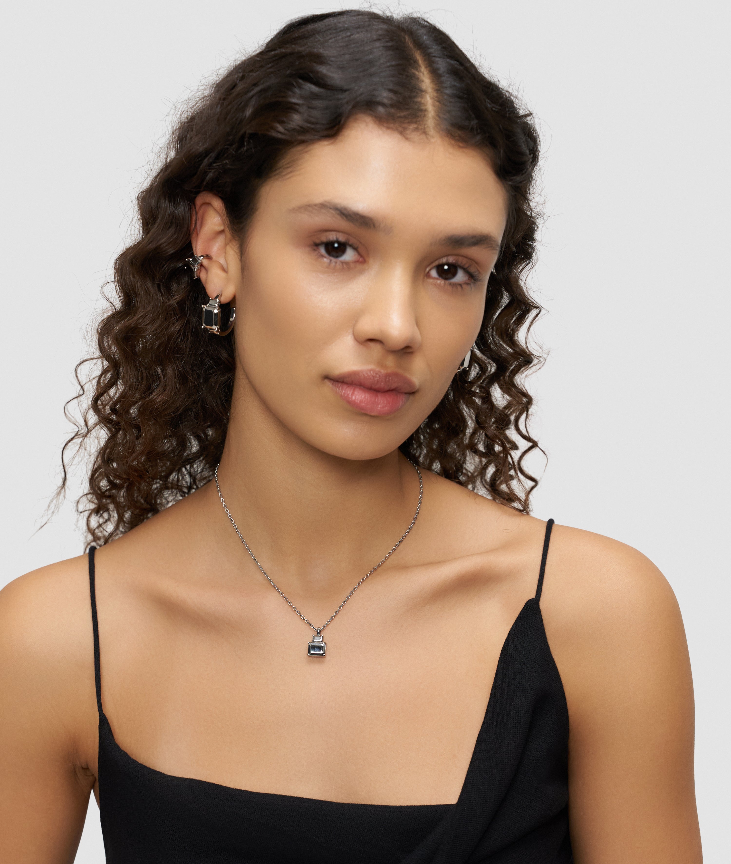 Frau mit gewelltem Haar trägt ein schwarzes Oberteil, den Liebeskind Berlin LIEBESKIND BERLIN Earcuff - Steel Diamond und eine passende Edelstahlkette und schaut in die Kamera.