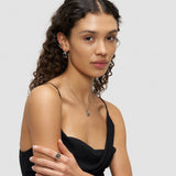 Frau mit lockigem Haar, die ein schwarzes Kleid, eine silberne Halskette, Ohrringe und den Liebeskind Berlin Ring - Steel Diamond in 54 trägt, posiert vor einem schlichten Hintergrund.