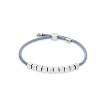 Das LIEBESKIND BERLIN Armband - Brick von Liebeskind Berlin besteht aus einem hellblauen Textilband mit silbernen Würfelperlen, die den Schriftzug LIEBESKIND tragen - ein auffälliges Stück aus der Armband-Kollektion, das auf weißem Hintergrund gezeigt wird.