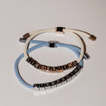 Zwei LIEBESKIND BERLIN Armbänder - Brick von Liebeskind Berlin, jeweils mit würfelförmigen Buchstabenperlen auf weißen und hellblauen Textilkordeln, sind ein stylisches Statement.