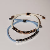 Zwei LIEBESKIND BERLIN Armbänder - Brick von Liebeskind Berlin, jeweils mit würfelförmigen Buchstabenperlen auf weißen und hellblauen Textilkordeln, sind ein stylisches Statement.
