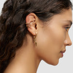 Frau mit gewelltem Haar trägt ein stilvolles Liebeskind Berlin Urban Chic Earcuff Set und mehrere goldene Ohrringe, darunter baumelnde Modelle, an ihrem linken Ohr.