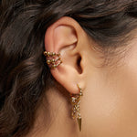 Nahaufnahme eines Ohrs, das das Liebeskind Berlin Earcuff Set - Urban Chic trägt: drei goldene Manschettenohrringe und ein goldener Creolenohrring mit baumelnden Anhängern.