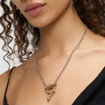 Eine Frau trägt die LIEBESKIND BERLIN Halskette - Urban Chic von Liebeskind Berlin im Bicolor-Look mit Knebelverschluss, Silberkette und goldenen Akzenten. Für ein zeitloses Design wird sie mit einem schwarzen Oberteil gestylt.