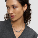 Eine Frau mit lockigem Haar, die ein graues Oberteil, silberne Ohrringe und die Liebeskind Berlin Halskette - Twist trägt, schaut zur Seite.
