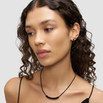 Frau mit lockigem Haar, die die LIEBESKIND BERLIN Halskette - Twist von Liebeskind Berlin und Ohrringe trägt und in einem schwarzen Spaghettiträgertop nach unten schaut.