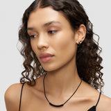Frau mit lockigem Haar, die die LIEBESKIND BERLIN Halskette - Twist von Liebeskind Berlin und Ohrringe trägt und in einem schwarzen Spaghettiträgertop nach unten schaut.