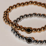 Liebeskind Berlin Perlen - Stahlperlen: Zwei Perlenarmbänder, eines in Gold und eines in Silber, mit runden Perlen in der Mitte, auf denen "LIEBESKIND BERLIN" eingraviert ist - ein stilvolles, elegantes Accessoire-Set.