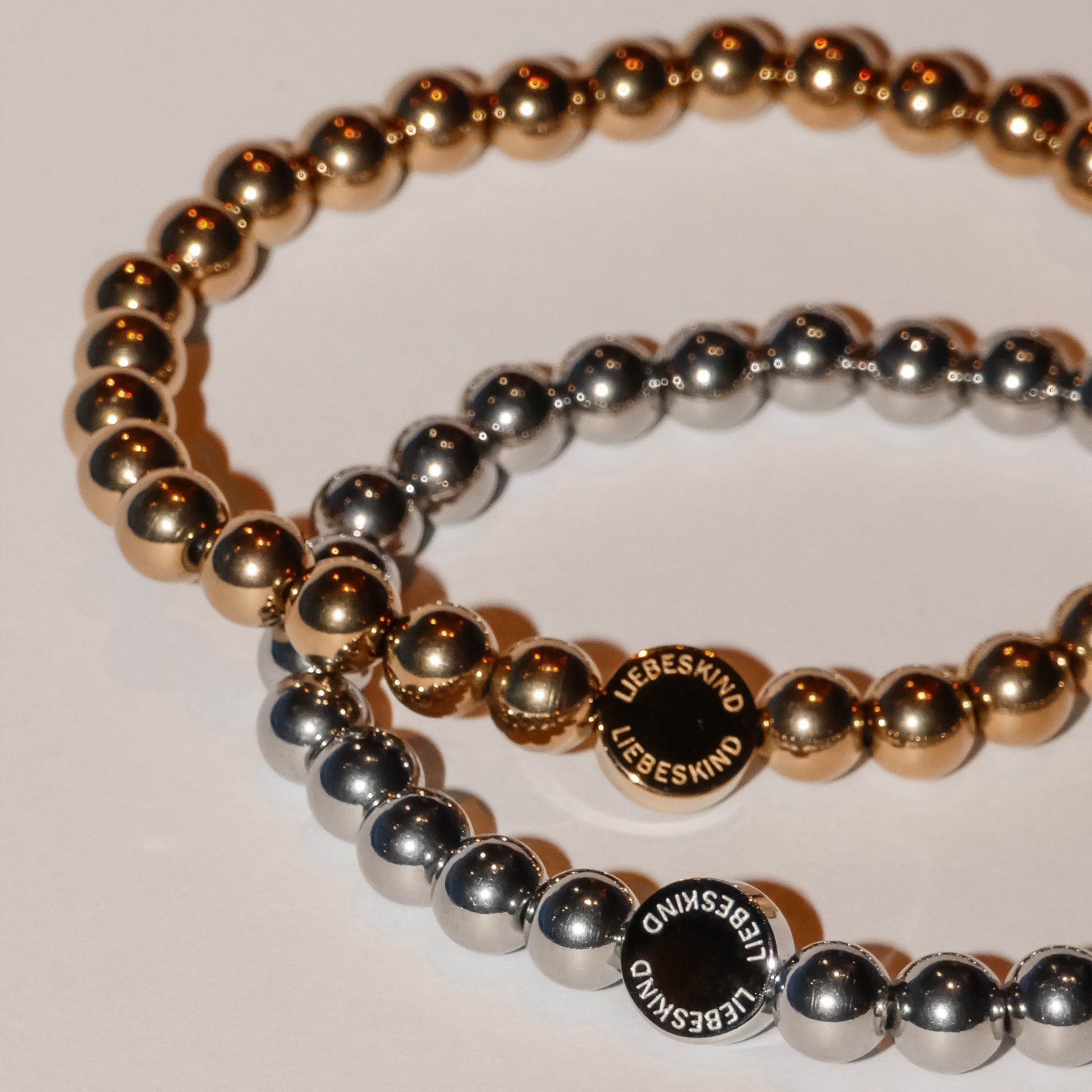 Liebeskind Berlin Perlen - Stahlperlen: Zwei Perlenarmbänder, eines in Gold und eines in Silber, mit runden Perlen in der Mitte, auf denen "LIEBESKIND BERLIN" eingraviert ist - ein stilvolles, elegantes Accessoire-Set.