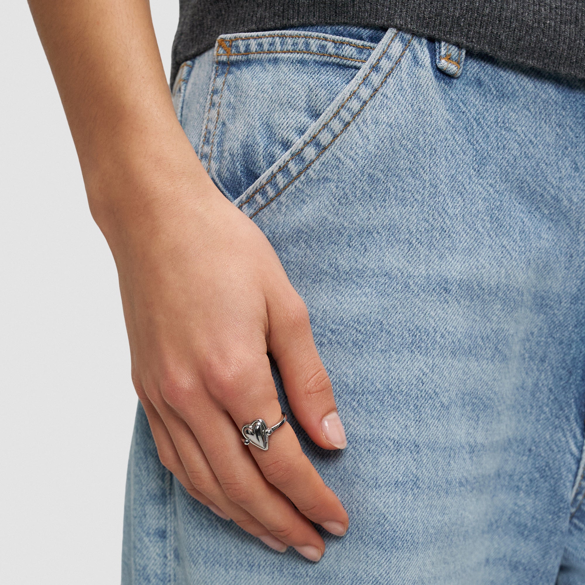 Eine Person in hellblauer Jeans trägt den Liebeskind Berlin Ring - Metal Heart in 54, die Hand in der Nähe der Hosentasche - ein stilvolles Geschenk für jemand Besonderen.