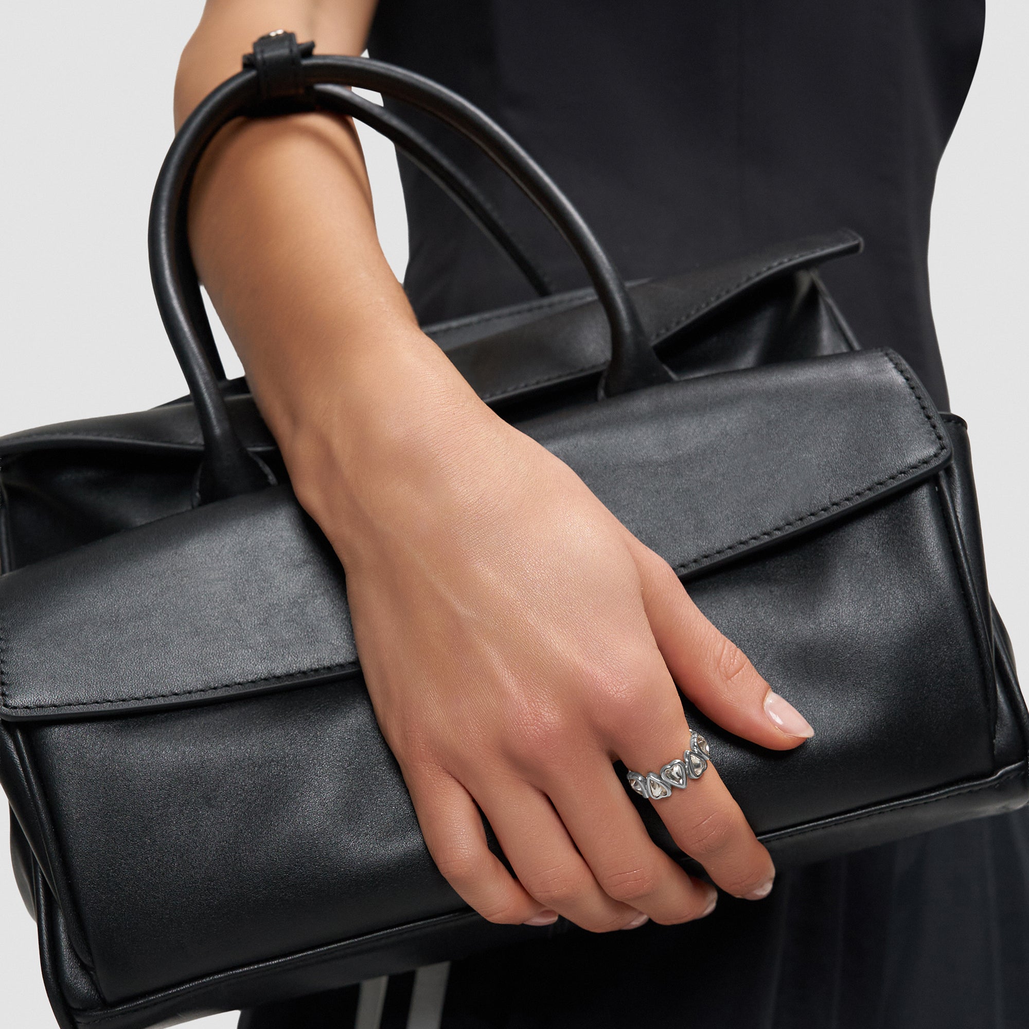 Eine Person hält eine schwarze Lederhandtasche und trägt den Liebeskind Berlin Ring - Glass Heart in 54, ein echtes Statement-Stück.