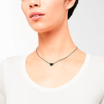 Eine Frau trägt ein weißes Hemd mit dem Liebeskind Berlin Set - Broken Heart: eine schwarze herzförmige Halskette an einer dünnen schwarzen Kordel und elegante roségoldene Ohrringe, die einen eleganten Look von Liebeskind Berlin ergeben.