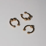 Drei goldene runde Ohrringe mit Kugelenden aus dem LIEBESKIND BERLIN Earcuff Set - Urban Chic von Liebeskind Berlin sind auf einer weißen Fläche platziert.
