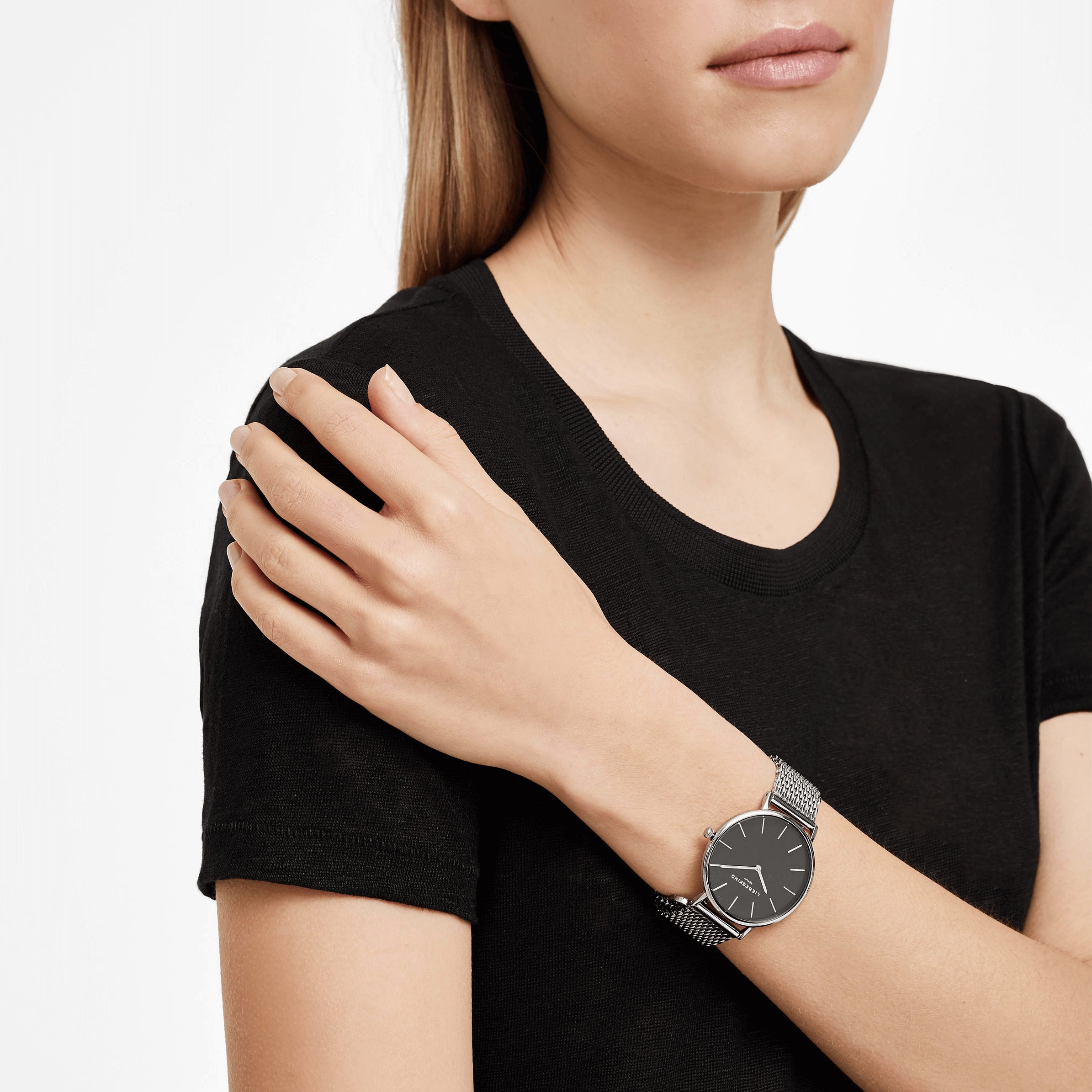 Eine Frau in einem schwarzen T-Shirt trägt das Liebeskind Berlin Set - Lovely Silver Basic mit einer eleganten Uhr mit schwarzem Zifferblatt und einem eleganten Herzarmband für einen mühelos schicken Look.