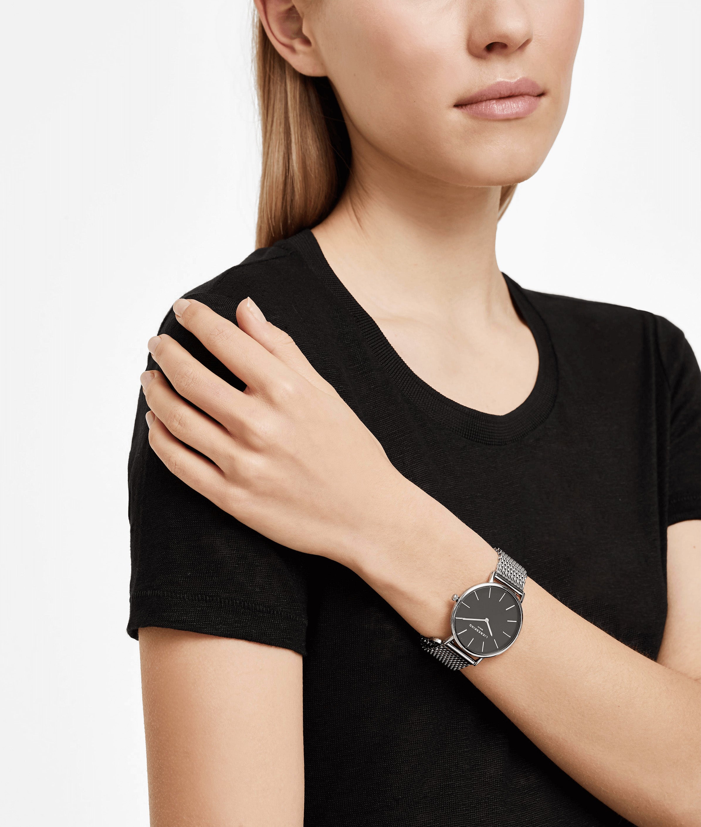 Eine Frau in einem schwarzen T-Shirt trägt das Liebeskind Berlin Set - Lovely Silver Basic mit einer eleganten Uhr mit schwarzem Zifferblatt und einem eleganten Herzarmband für einen mühelos schicken Look.