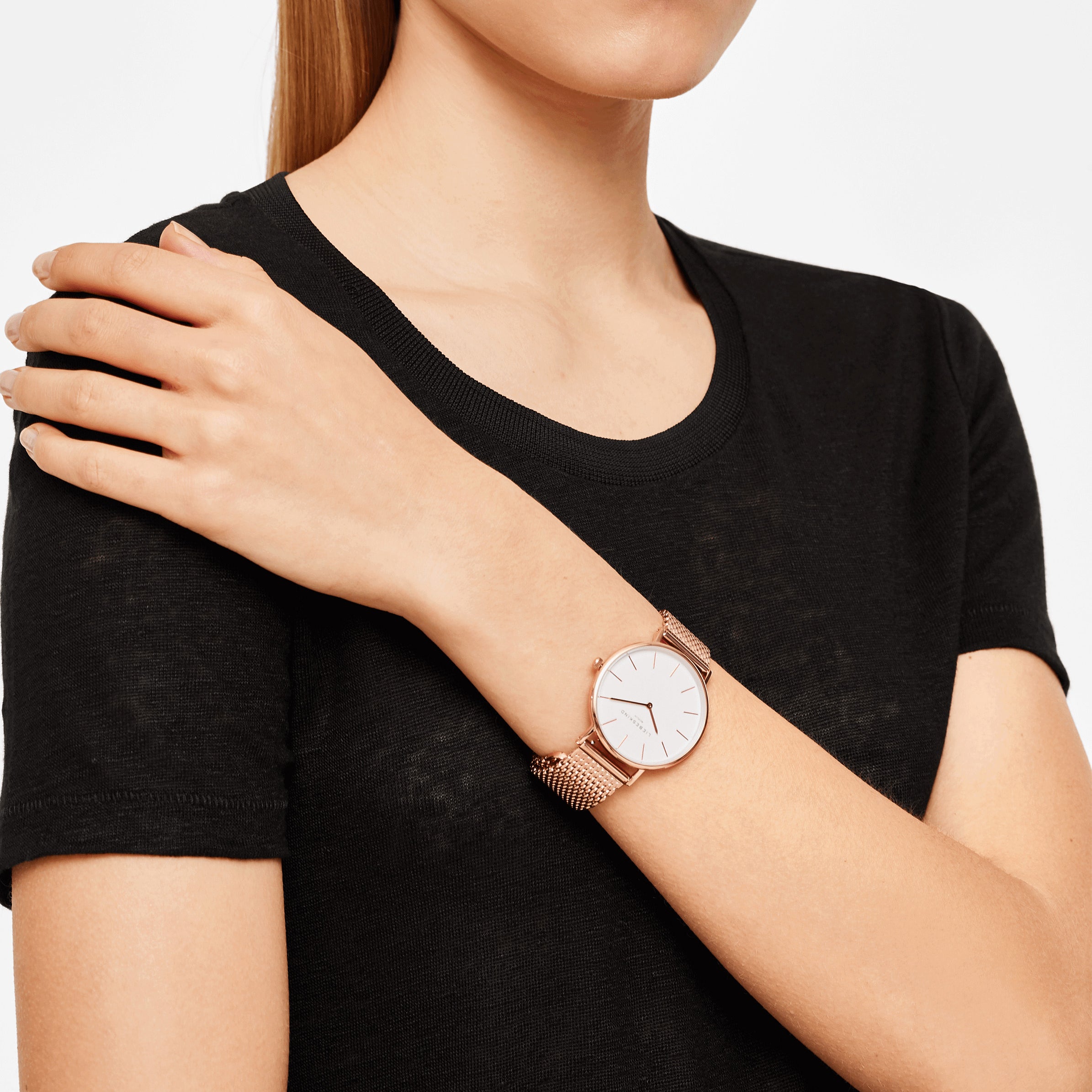 Eine Frau in einem schwarzen T-Shirt trägt das Liebeskind Berlin Set - Roségold Broken Heart und stützt ihre Hand auf die gegenüberliegende Schulter, um einen schicken, minimalistischen Look zu kreieren.
