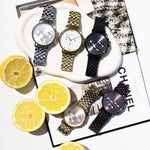Five wristwatches, featuring the LIEBESKIND BERLIN Armbanduhr – Modern Chronograph and elegant Damenuhr styles, in silver, gold, black, and two-tone finishes, are displayed on books and a tray with halved lemons in a brightly lit scene.