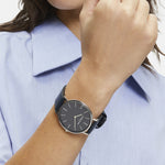 Eine Person in einem blauen Hemd trägt die LIEBESKIND BERLIN Armbanduhr - Skandinavian Classic von Liebeskind Berlin mit einem Lederriemen und hält die Faust erhoben neben dem Gesicht.