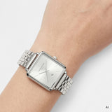 ki generierte Detailaufnahme einer LIEBESKIND BERLIN Damen Armbanduhr mit eckigem Gehäuse, silberfarbenem Zifferblatt, Datumsanzeige und silberfarbenem Edelstahlarmband am Handgelenk getragen