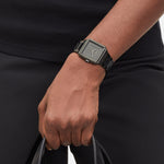 Eine Person in schlichter schwarzer Kleidung hält eine schwarze Tasche und trägt die LIEBESKIND BERLIN Armbanduhr - The Square Minimalist von Liebeskind Berlin.