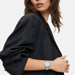 Frau in schwarzem Blazer schaut zur Seite und trägt eine Liebeskind Berlin Armbanduhr - The Round Staple mit modernem Design am linken Handgelenk.