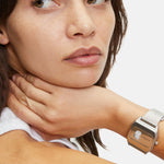 Eine Frau mit braunen Haaren schaut weg, das Kinn auf die Hand gestützt, sie trägt die LIEBESKIND BERLIN Armbanduhr - Vinyl Vision von Liebeskind Berlin mit einem eleganten Edelstahlgehäuse.