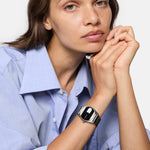 Frau in hellblauem Hemd trägt die Liebeskind Berlin Armbanduhr - Round Vinyl Vision mit verspiegeltem Zifferblatt und stützt ihr Kinn auf die Hände.