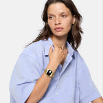 Frau in hellblauem Hemd trägt die LIEBESKIND BERLIN Armbanduhr - Round Vinyl Vision von Liebeskind Berlin mit verspiegeltem Ziffernblatt und einem Ring, während sie zur Seite blickt.